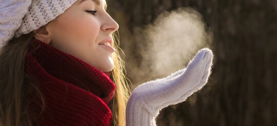 Frau steht im Winter, der als schwierige Zeit für schuppige Hauterkrankungen gilt, draußen und atmet aus.