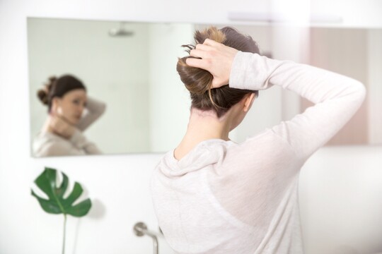 Frau mit Psoriasis betrachtet sich im Spiegel