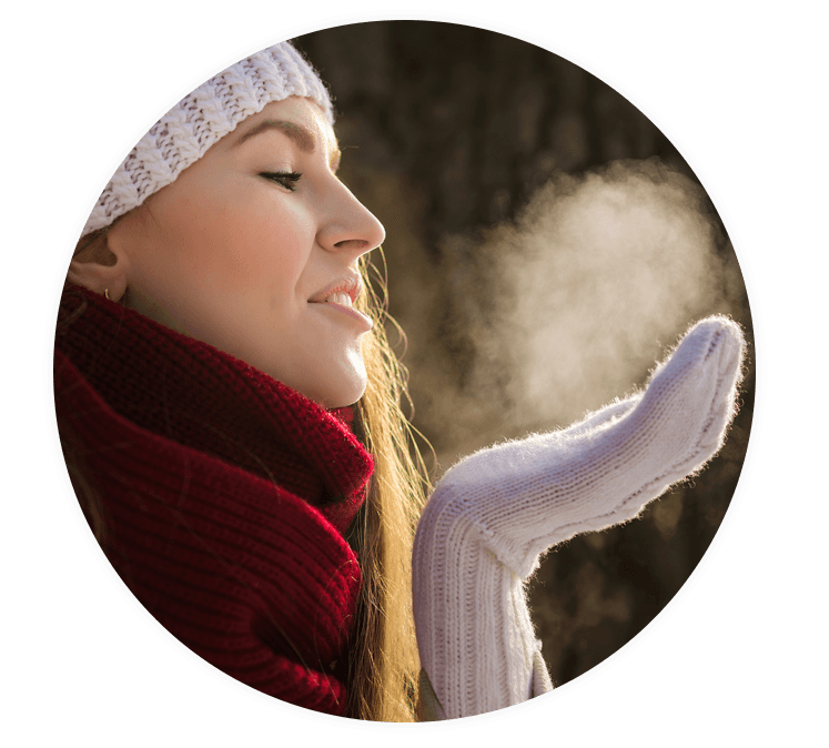 Frau steht im Winter, der als schwierige Zeit für schuppige Hauterkrankungen gilt, draußen und atmet aus.